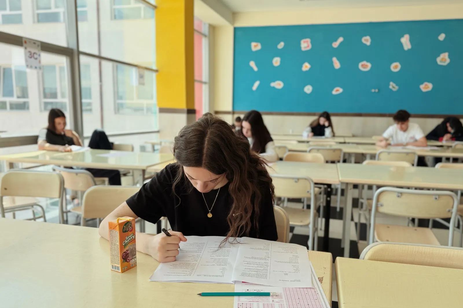 A student works through an exam paper at a classroom desk