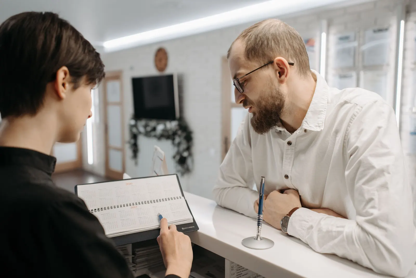 A receptionist and a client go over an appointment book at a clinic front desk