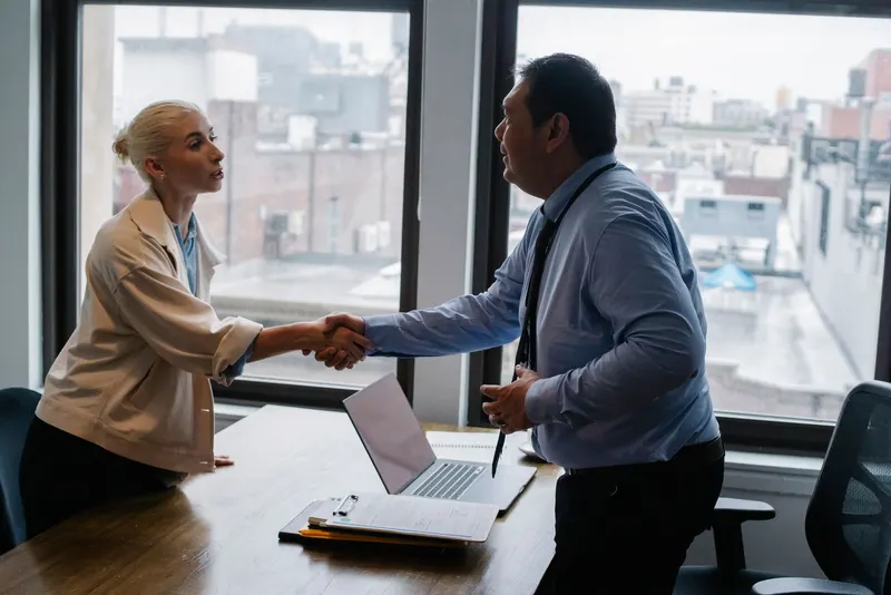 A candidate shakes hands with an interviewer across a desk