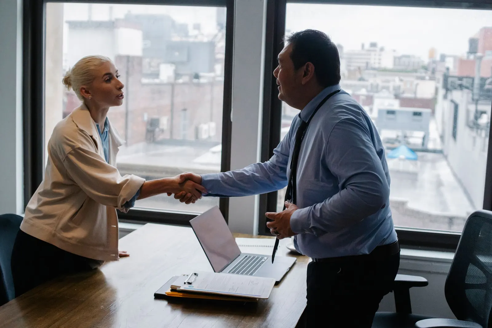 A candidate shakes hands with an interviewer across a desk in an office